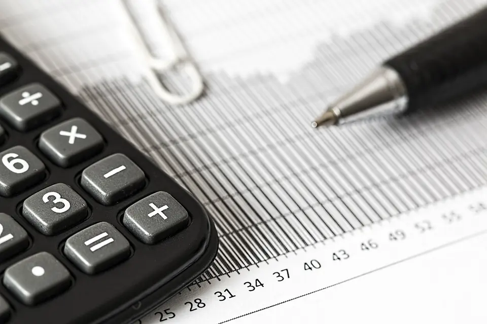 A calculator and pen resting on a printed column of ruled bookkeeping figures.